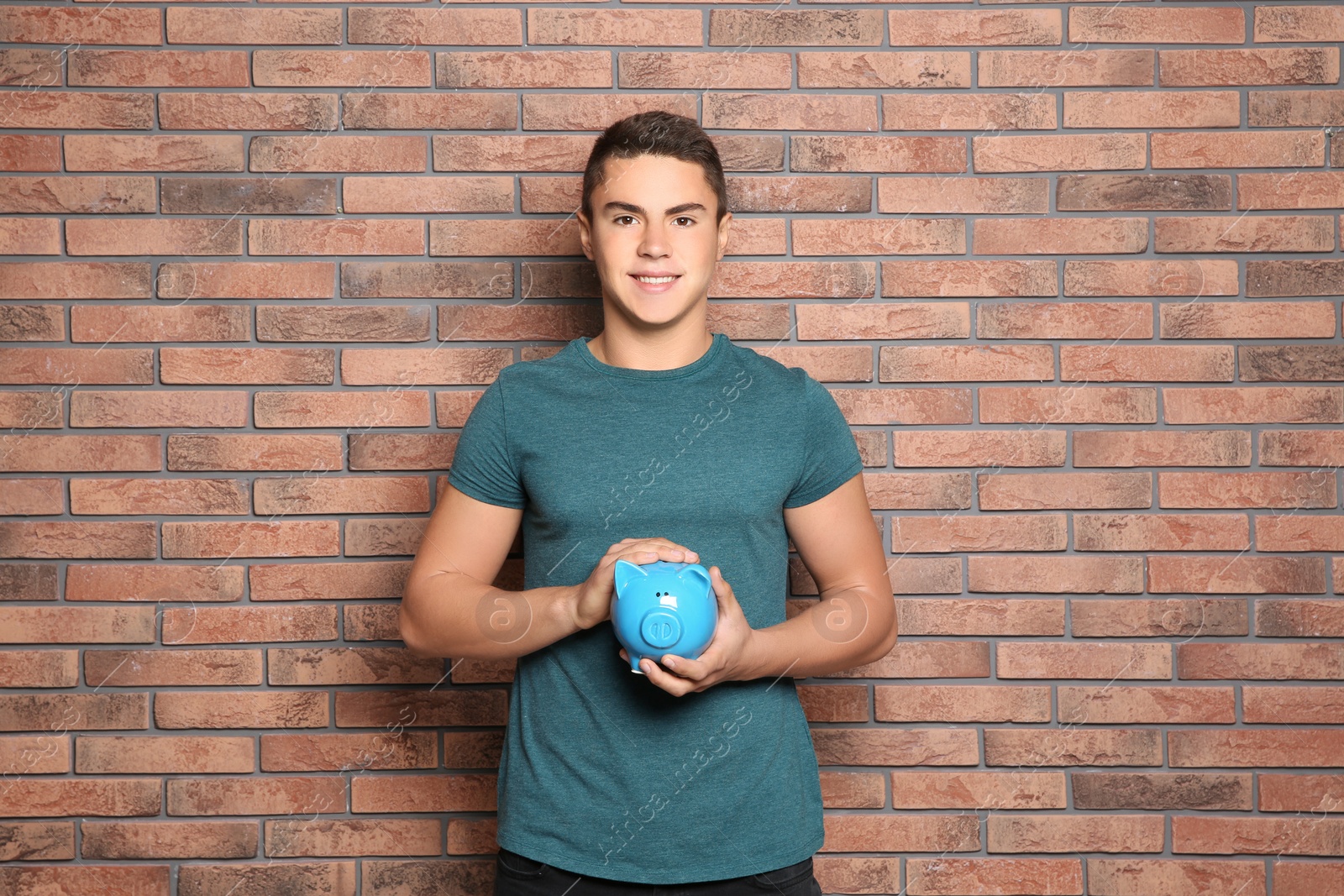 Photo of Teenage boy with piggy bank near brick wall