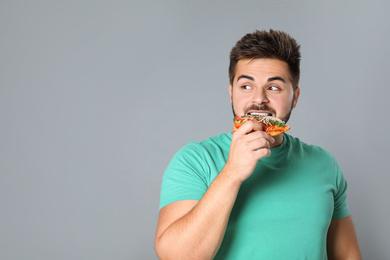 Handsome man with pizza on grey background, space for text