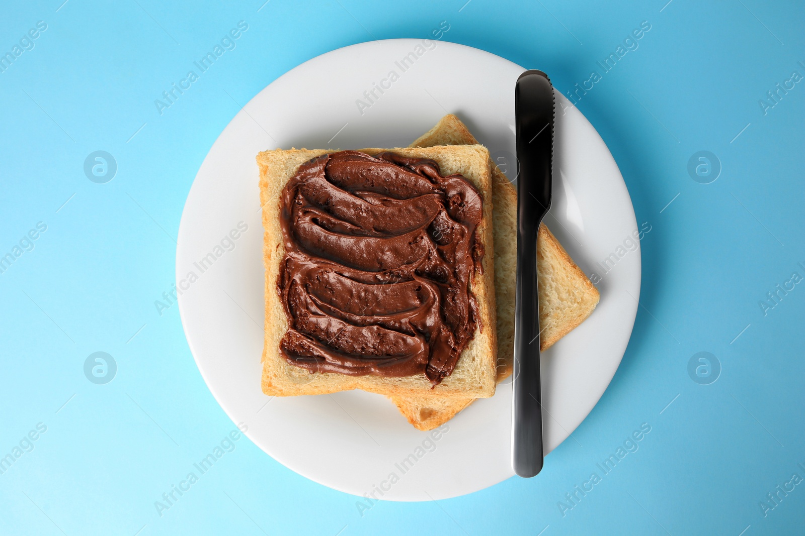 Photo of Tasty toast with chocolate paste on light blue background, top view