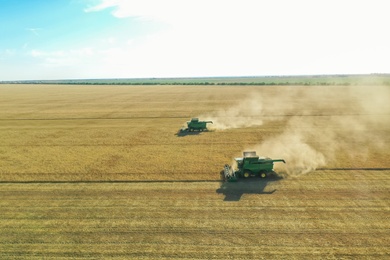 Photo of Beautiful aerial view of modern combine harvesters working in field on sunny day. Agriculture industry