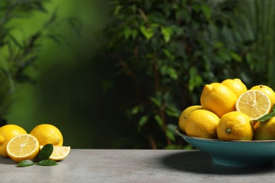 Photo of Fresh lemons and green leaves on grey table outdoors. Space for text