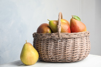 Photo of Ripe juicy pears in wicker basket on wooden table against light background