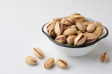 Photo of Bowl and pistachio nuts on white background, space for text