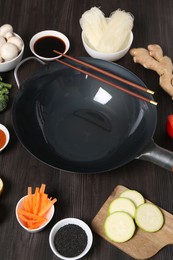 Photo of Empty iron wok and chopsticks surrounded by ingredients on dark grey wooden table