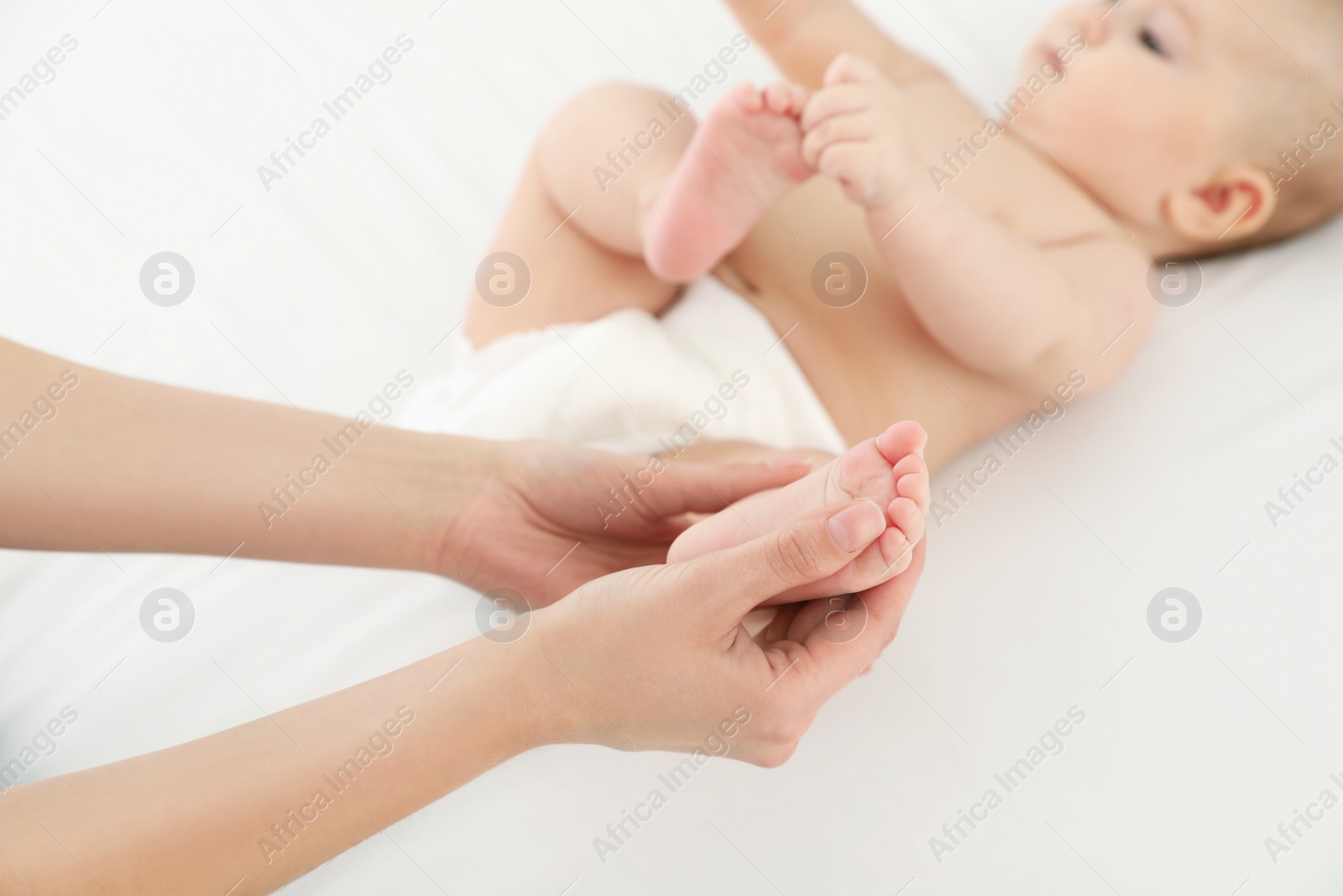 Photo of Mother and her cute child on white bed, closeup. Baby massage and exercises