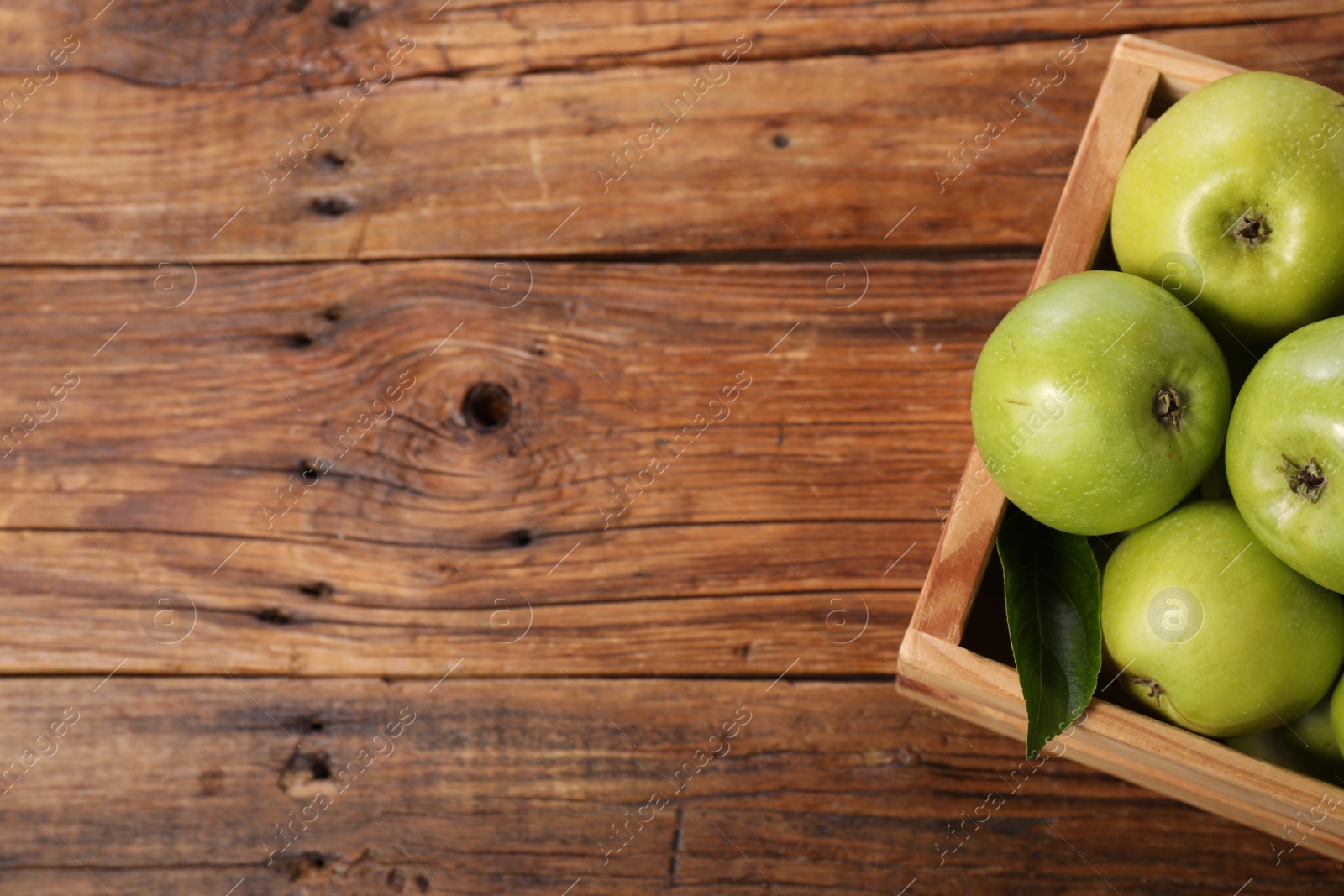 Photo of Fresh ripe green apples in crate on wooden table, top view. Space for text