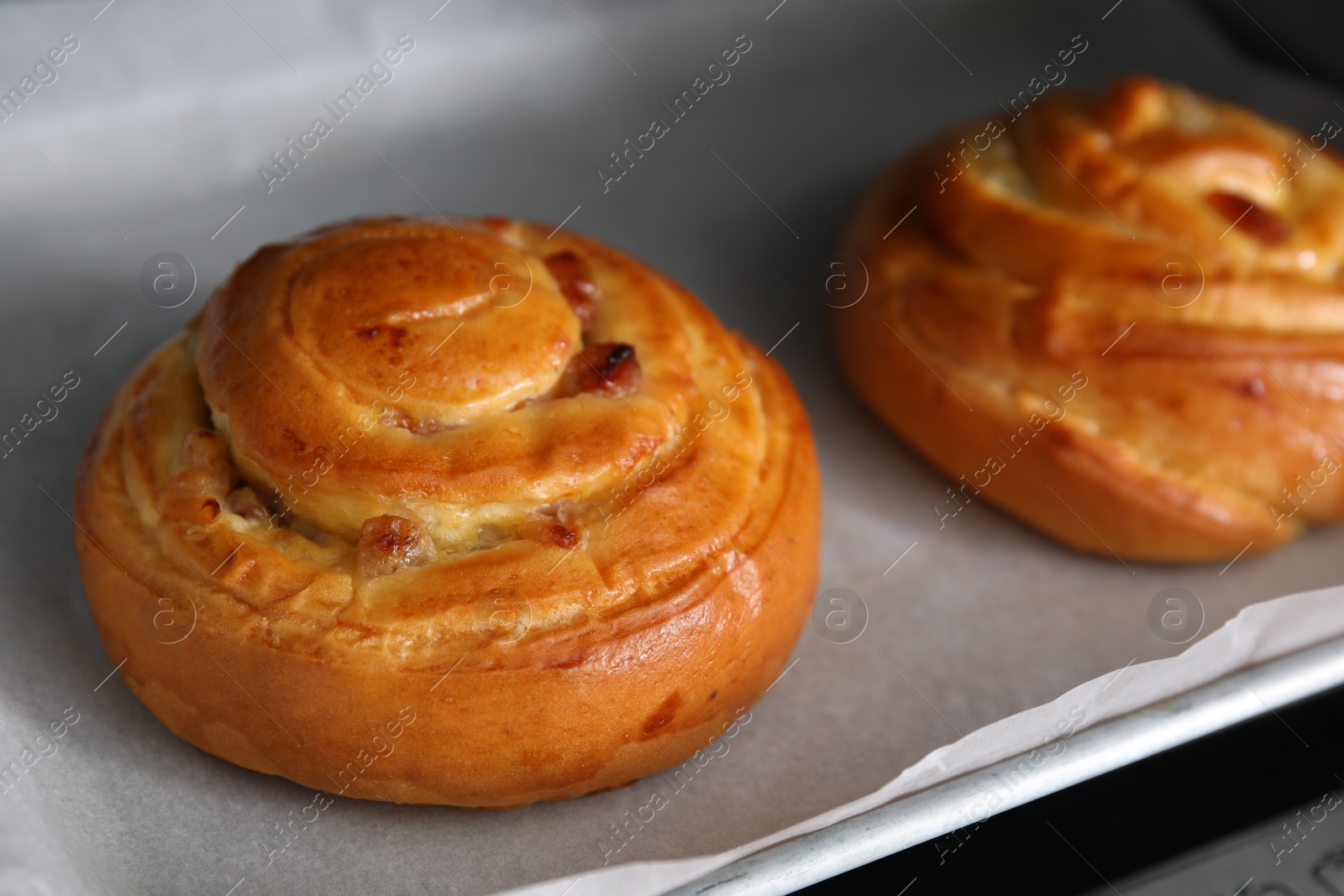 Photo of Delicious rolls with raisins on baking tray, closeup. Cooking sweet buns