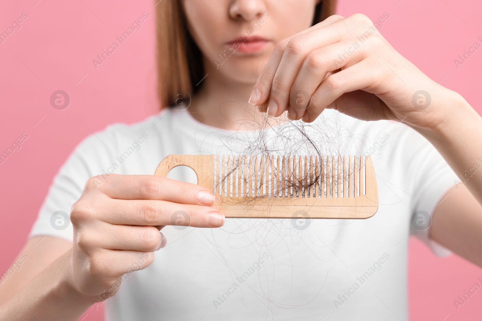 Photo of Woman untangling her lost hair from comb on pink background, closeup. Alopecia problem