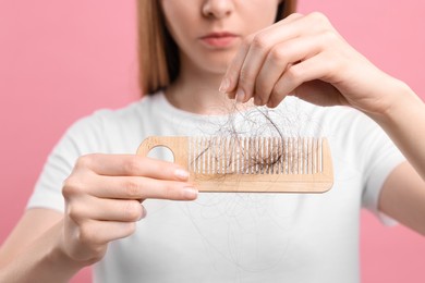 Woman untangling her lost hair from comb on pink background, closeup. Alopecia problem