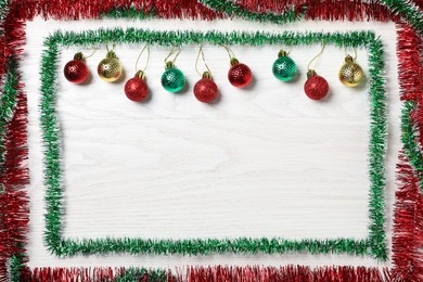 Frame of bright tinsel and Christmas balls on white wooden background, flat lay. Space for text