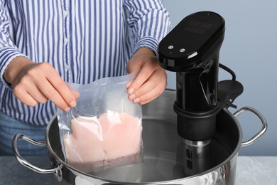 Photo of Woman putting vacuum packed meat into pot with thermal immersion circulator, closeup. Sous vide cooking