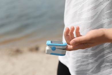 Photo of Young woman checking pulse with medical device after training on beach, closeup. Space for text