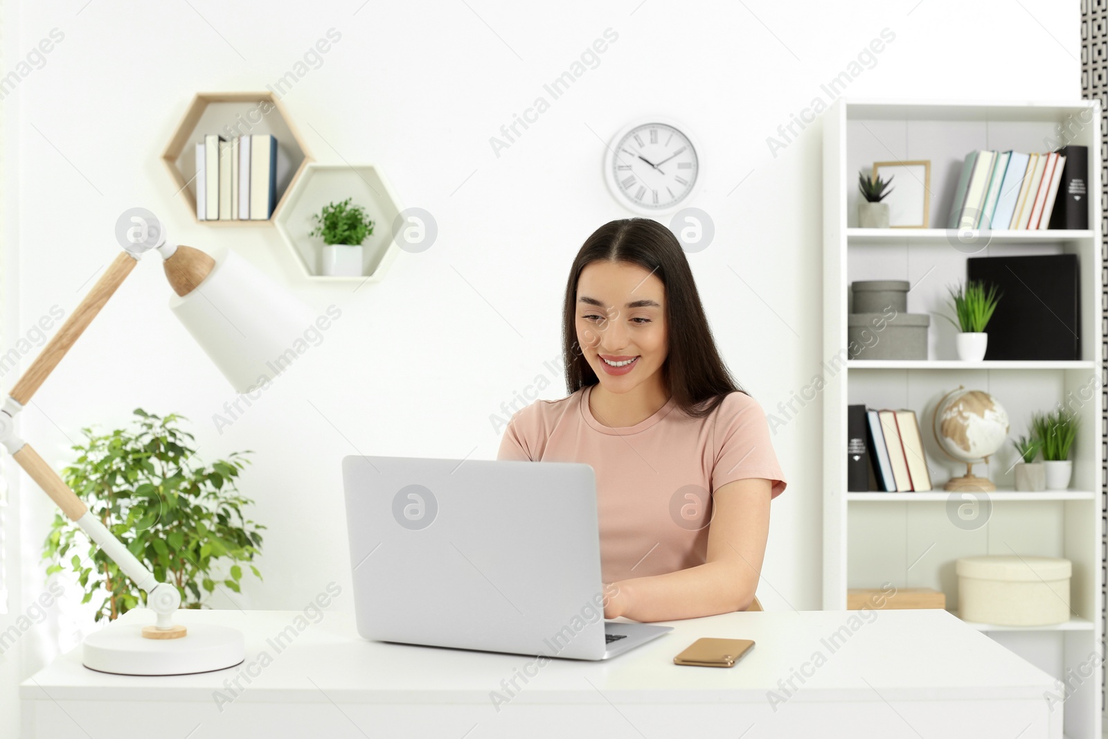 Photo of Home workplace. Woman working on laptop at white desk in room