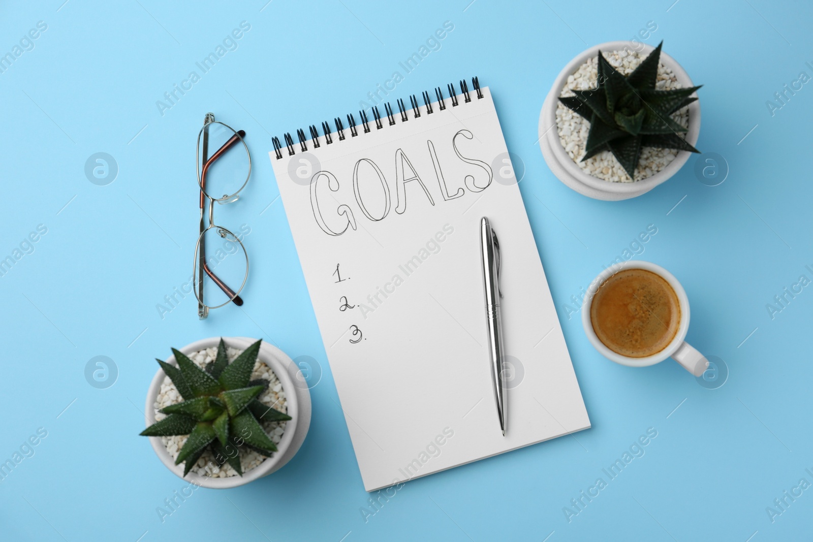 Photo of Planning concept. Flat lay composition with empty list of goals in notebook and glasses on light blue background