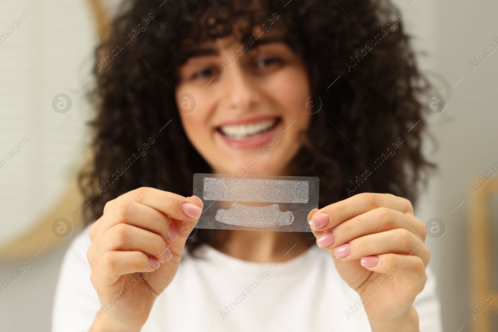 Photo of Young woman holding teeth whitening strips indoors, selective focus