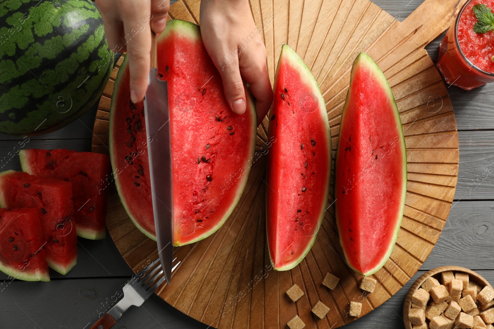 Photo of Woman cutting delicious watermelon at grey wooden table, top view
