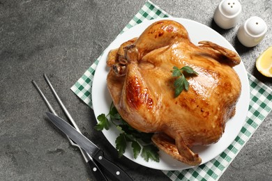 Photo of Tasty roasted chicken with parsley served on grey textured table, flat lay