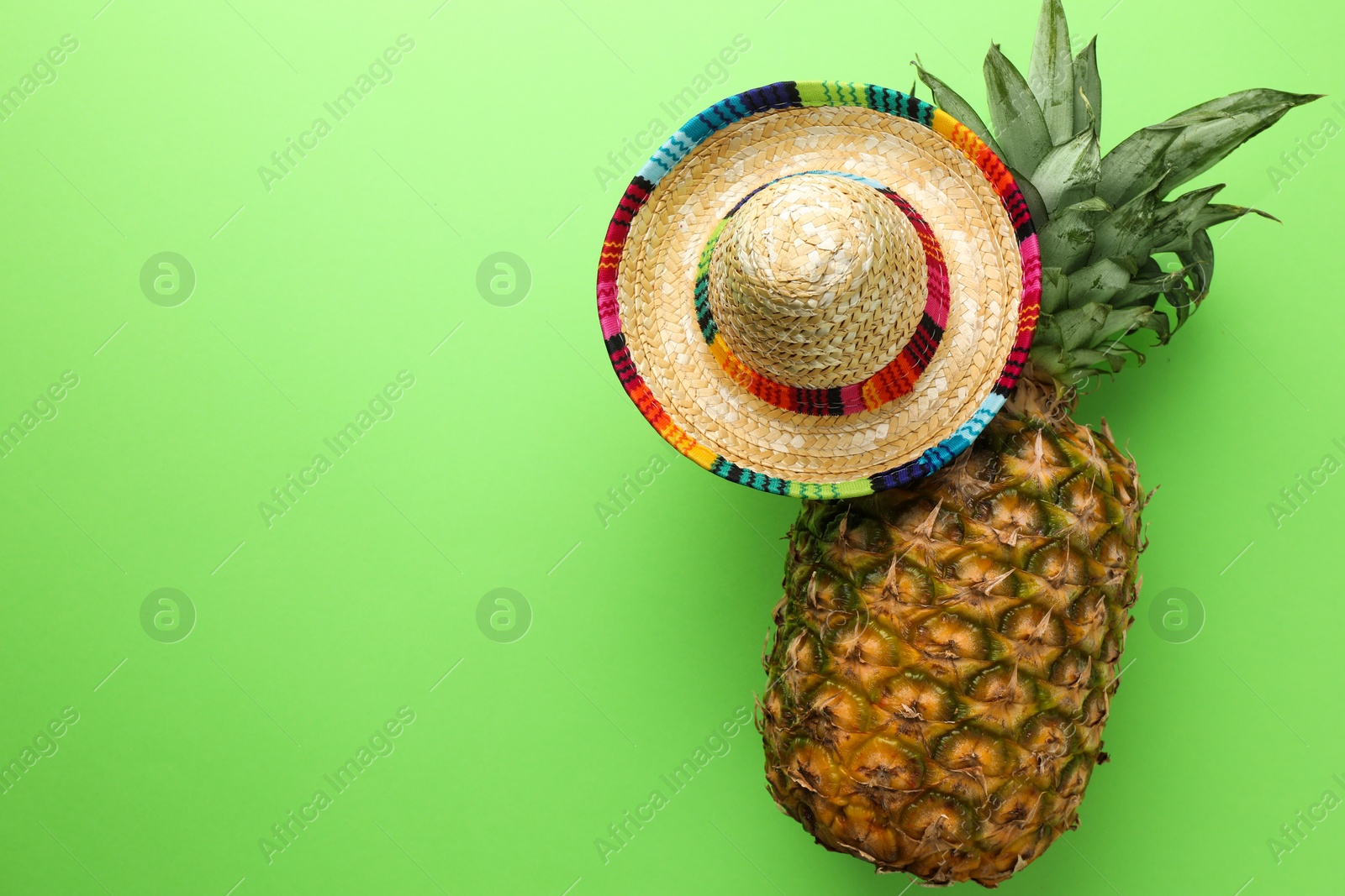 Photo of Mexican sombrero hat and pineapple on green background, top view. Space for text
