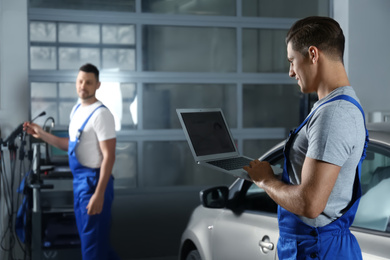 Photo of Mechanic with laptop doing car diagnostic at automobile repair shop. Space for text