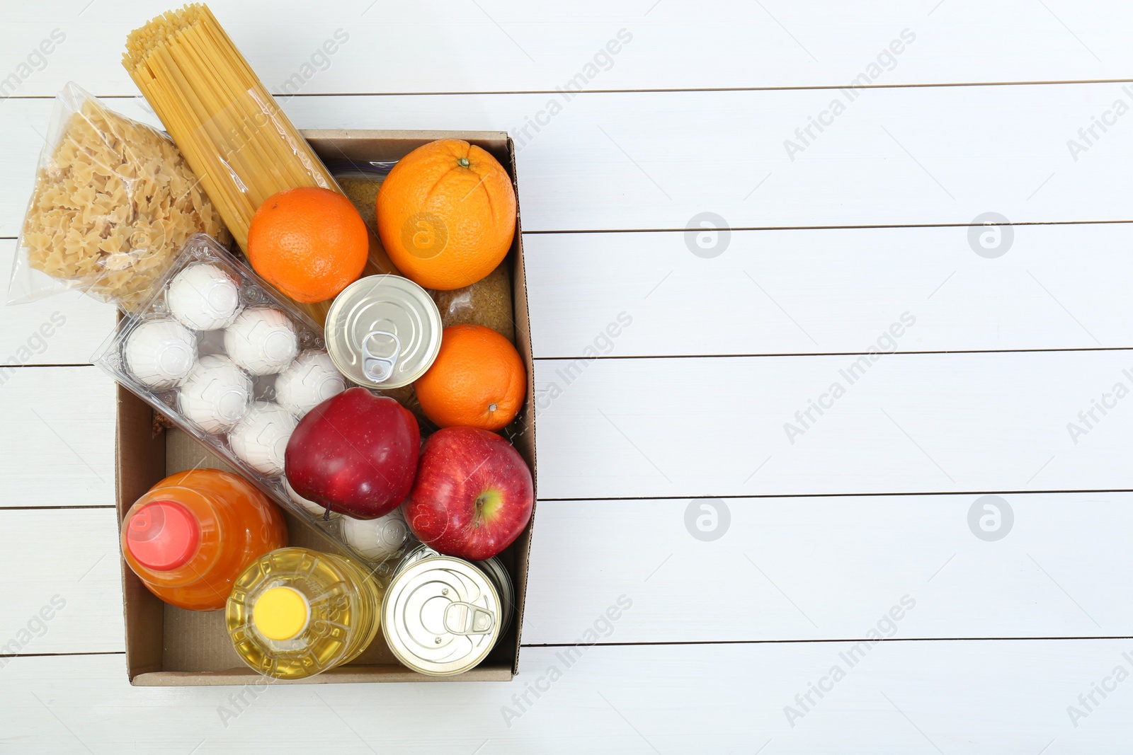 Photo of Humanitarian aid. Different food products for donation in box on white wooden table, top view. Space for text