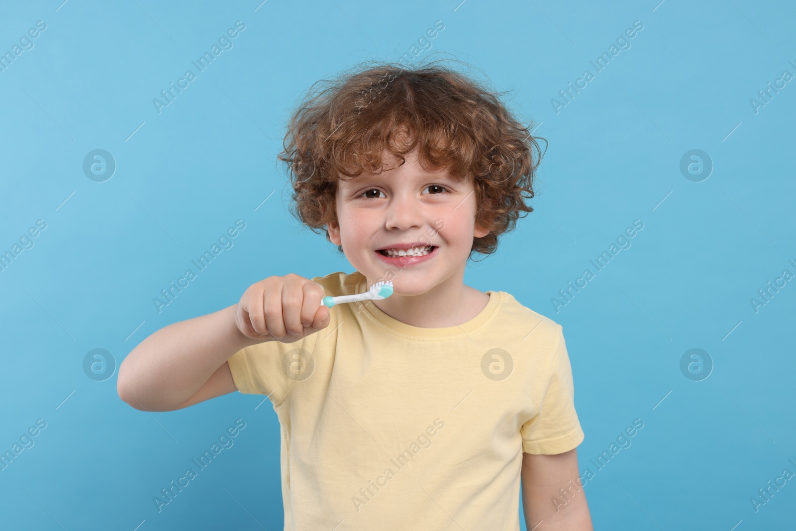 Photo of Cute little boy holding plastic toothbrush on light blue background