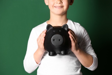 Photo of Little boy with piggy bank on color background, closeup