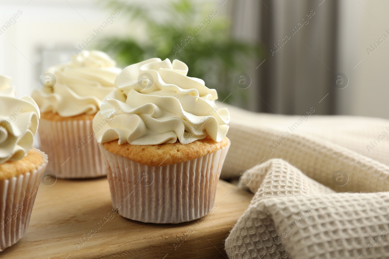 Photo of Tasty cupcakes with vanilla cream on wooden board, closeup