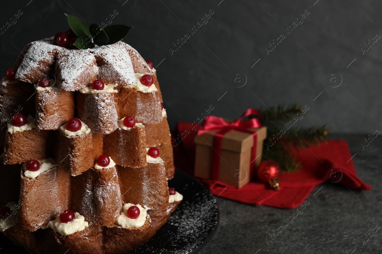 Photo of Delicious Pandoro Christmas tree cake with powdered sugar and berries near festive decor on black table, closeup. Space for text