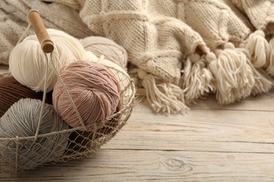 Photo of Soft woolen yarns and knitted fabric on white wooden table, closeup. Space for text
