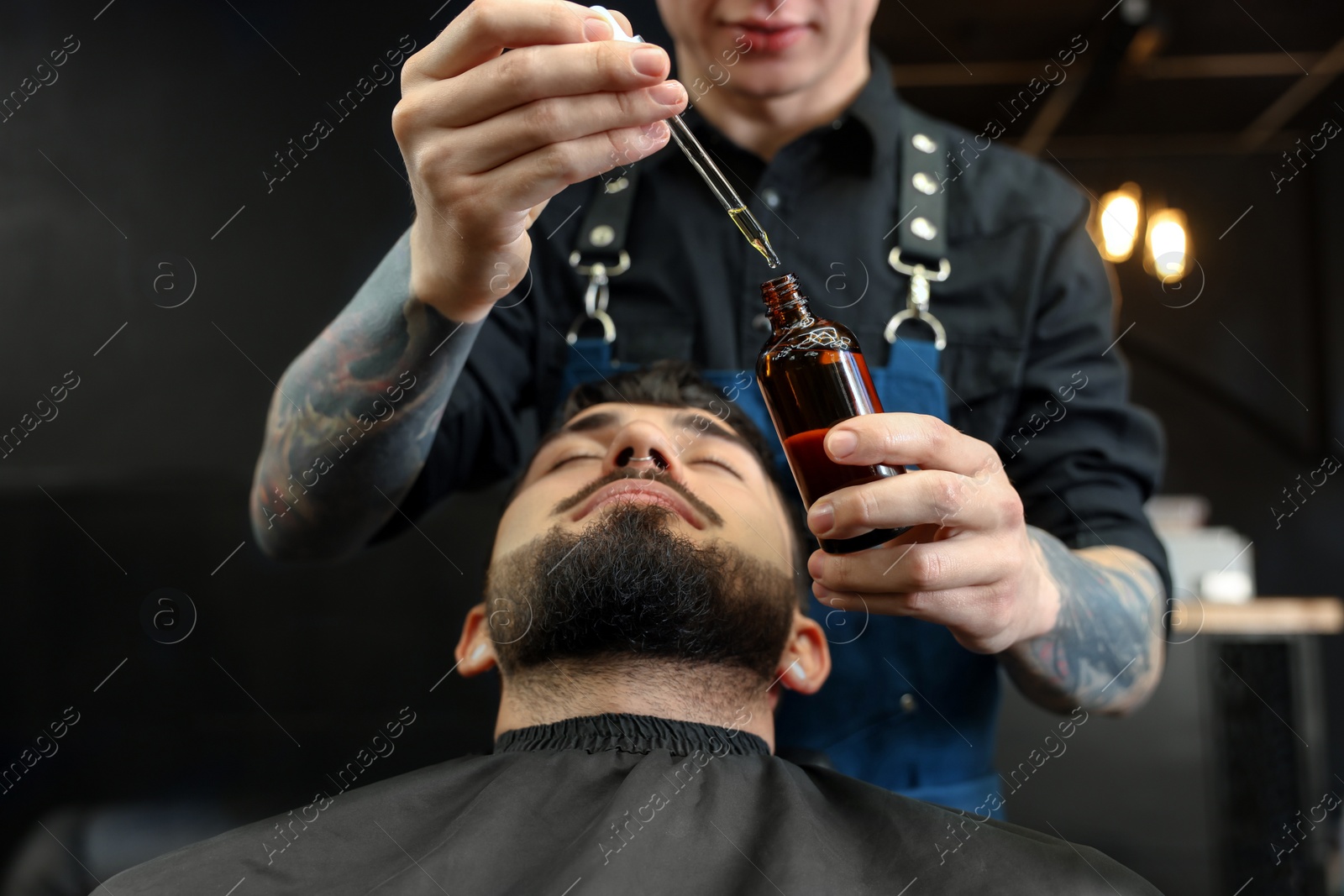 Photo of Hairdresser with beard oil near client in barbershop, closeup. Professional shaving service