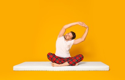 Photo of Man sitting on soft mattress and stretching against orange background