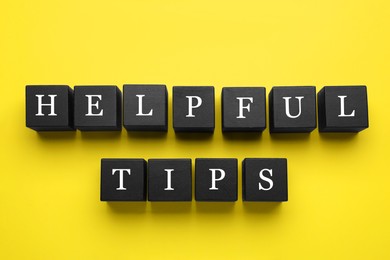 Photo of Phrase Helpful Tips made of black cubes with letters on yellow background, top view