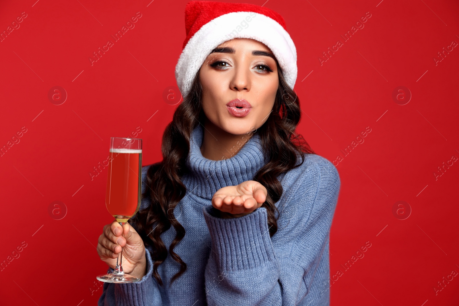 Photo of Beautiful woman in Santa hat holding glass of champagne on red background. Christmas party