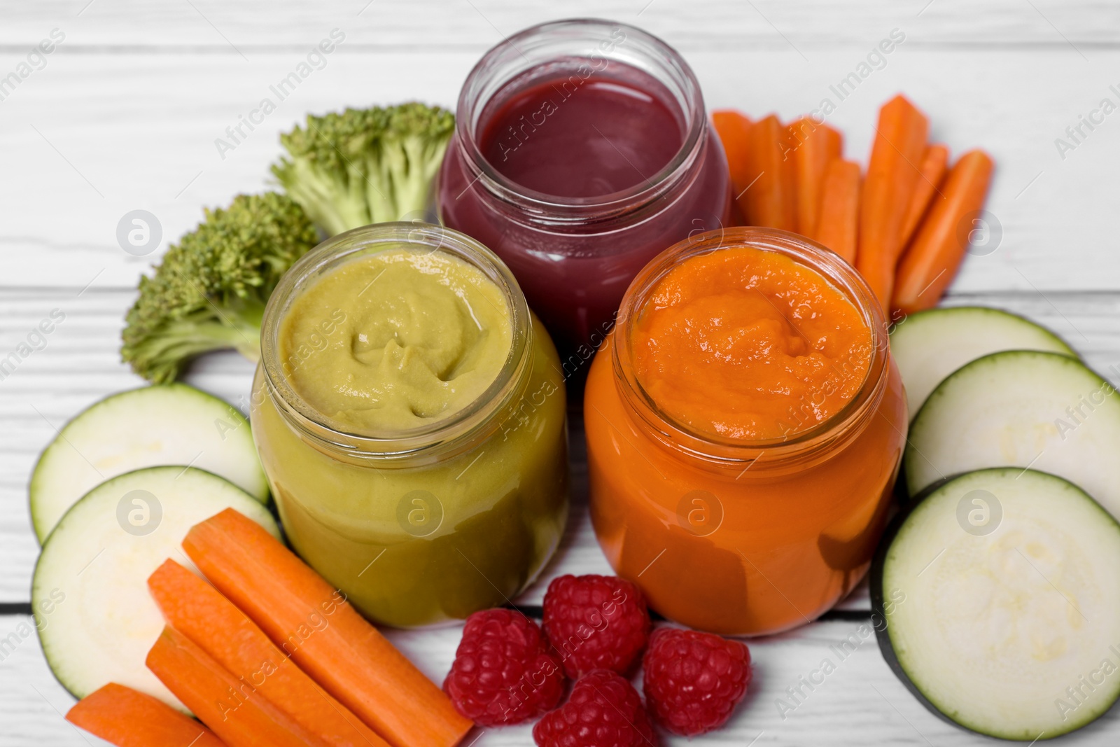 Photo of Jars with healthy baby food and ingredients on white wooden table