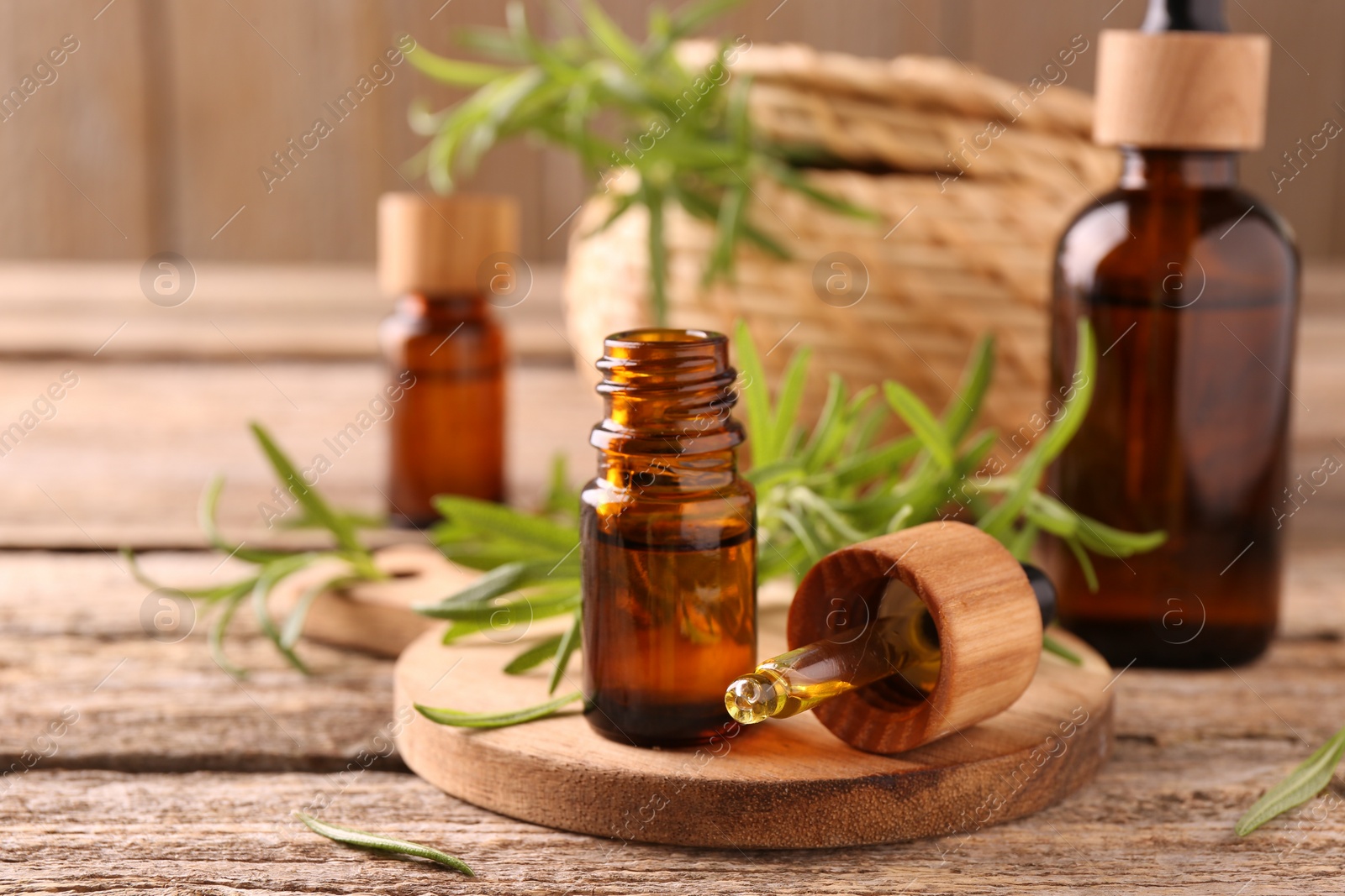 Photo of Aromatic essential oils in bottles, pipette and rosemary on wooden table, closeup