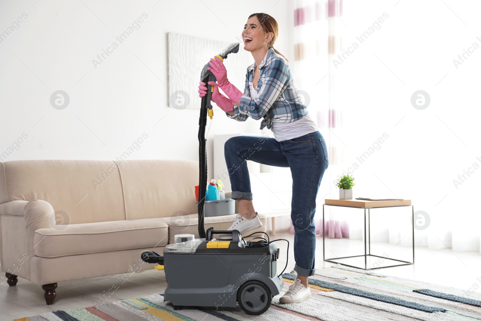 Photo of Happy young woman cleaning home with vacuum cleaner and having fun indoors