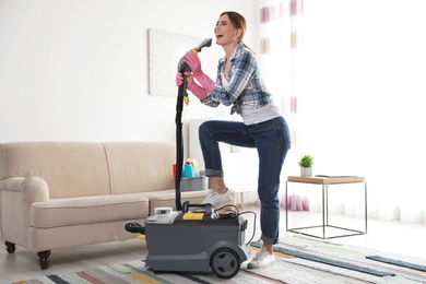 Photo of Happy young woman cleaning home with vacuum cleaner and having fun indoors