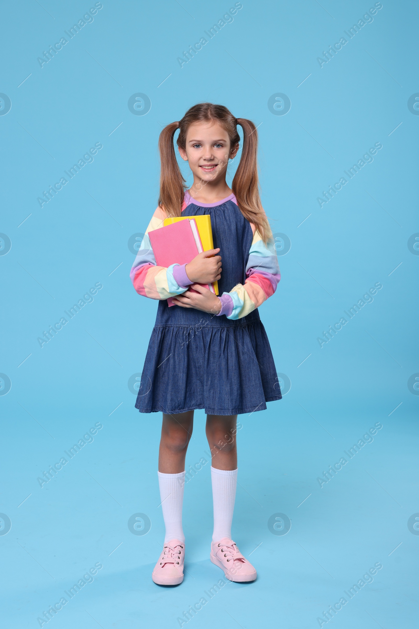 Photo of Happy schoolgirl with books on light blue background