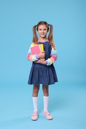 Photo of Happy schoolgirl with books on light blue background