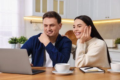 Photo of Happy couple with laptop shopping online at wooden table in kitchen