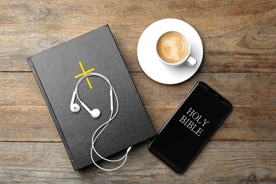Photo of Bible, phone, cup of coffee and earphones on wooden background, flat lay. Religious audiobook