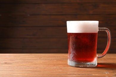 Photo of Glass mug with cold red beer on wooden table