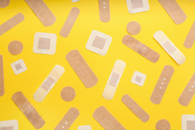 Different types of sticking plasters on yellow background, flat lay