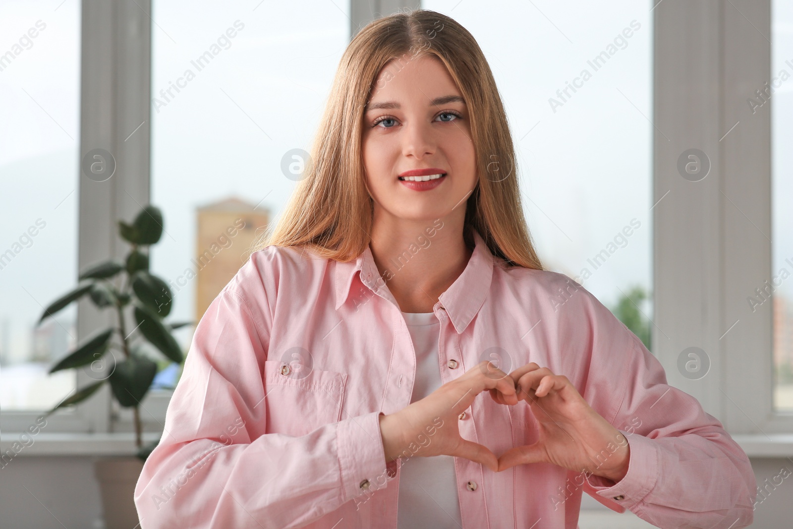 Photo of Young woman making heart with hands indoors. Volunteer concept