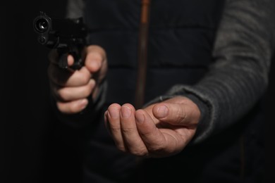 Photo of Dangerous criminal with gun on black background, closeup. Armed robbery