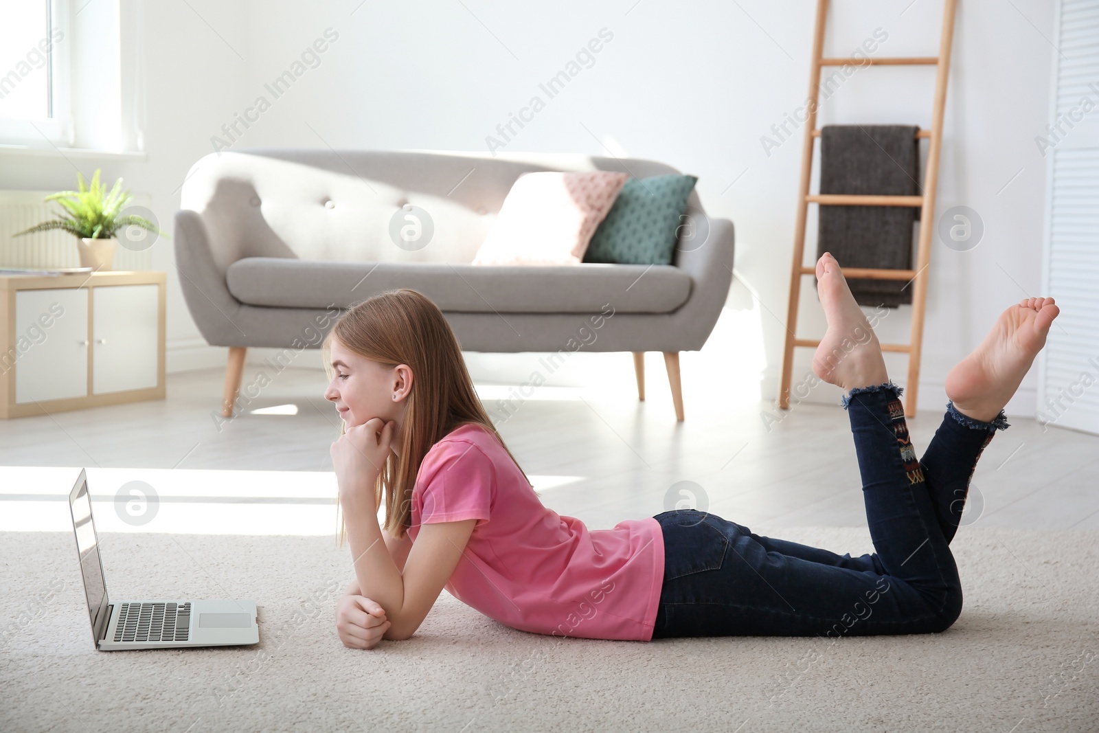 Photo of Teenage girl with laptop lying on cozy carpet at home