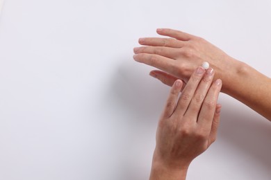 Photo of Woman applying cosmetic cream onto hand on white background, top view. Space for text
