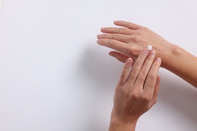 Woman applying cosmetic cream onto hand on white background, top view. Space for text