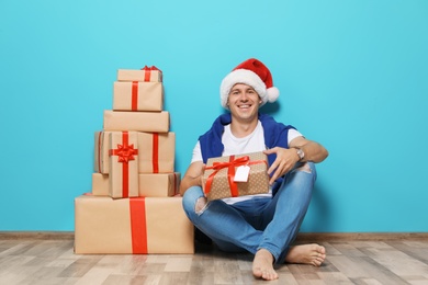 Photo of Young man with Christmas gifts near color wall