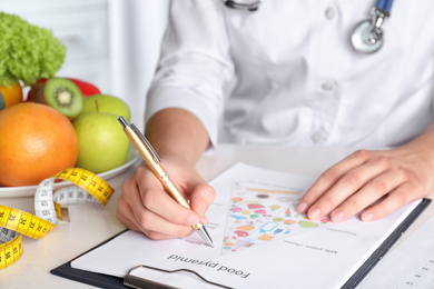 Photo of Female nutritionist with food pyramid chart at table, closeup